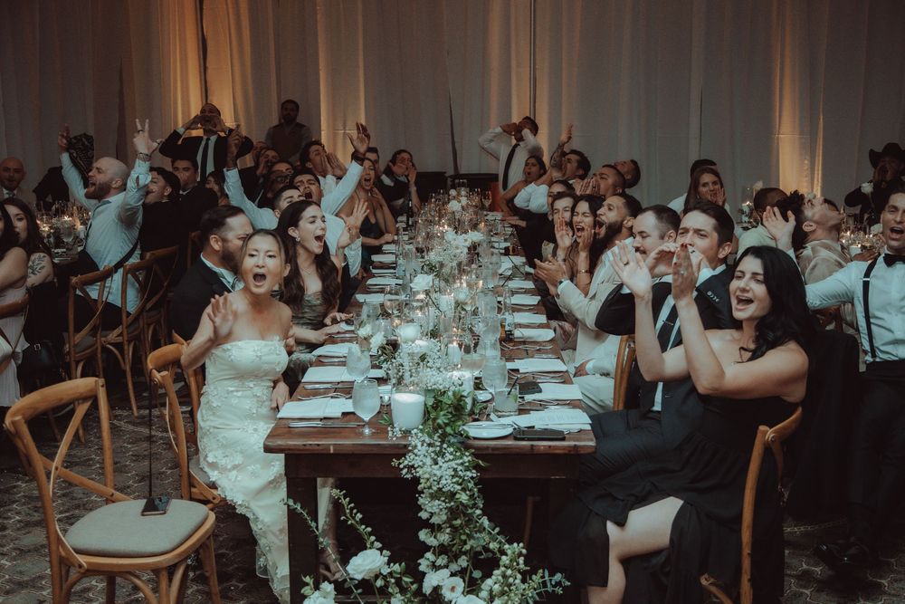 Bride and wedding guests laugh and celebrate joyfully at a elegantly decorated reception dinner table.
