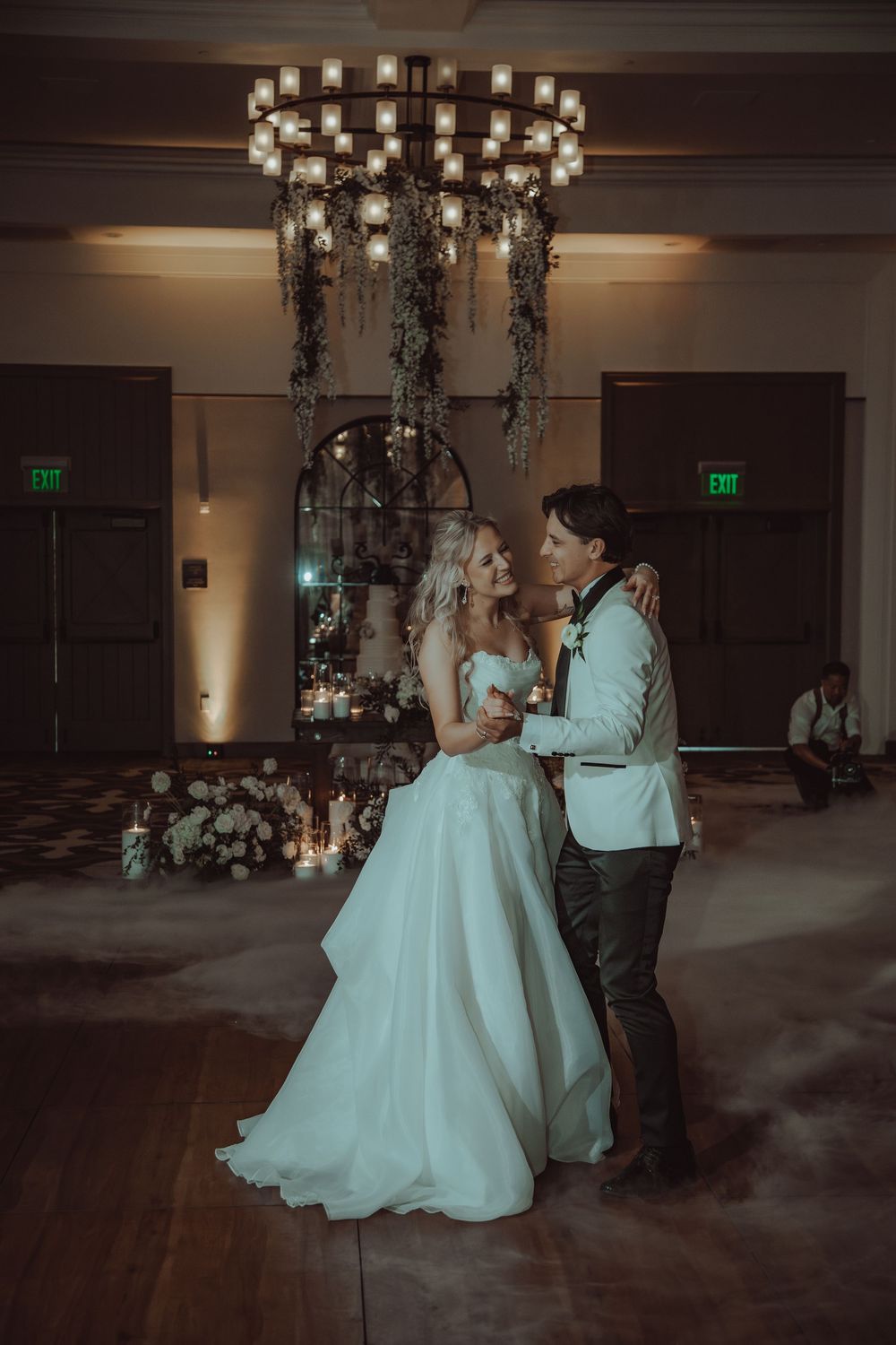 Bride and groom share their first dance under a chandelier with fog on the dance floor at an elegant wedding reception.