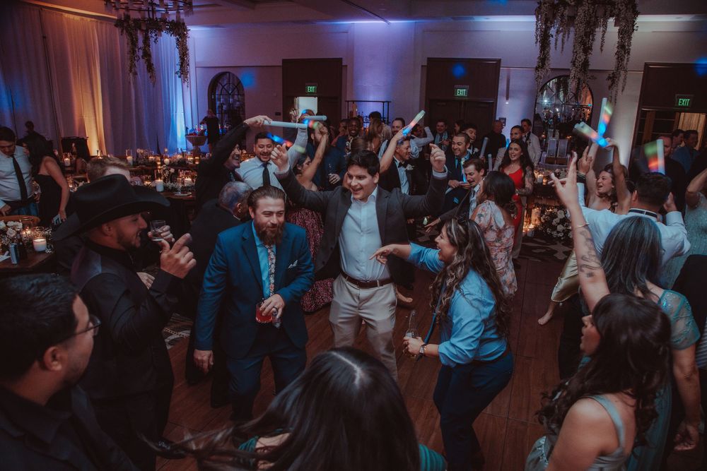 Wedding guests energetically dance together on a crowded dance floor during a lively wedding reception party.