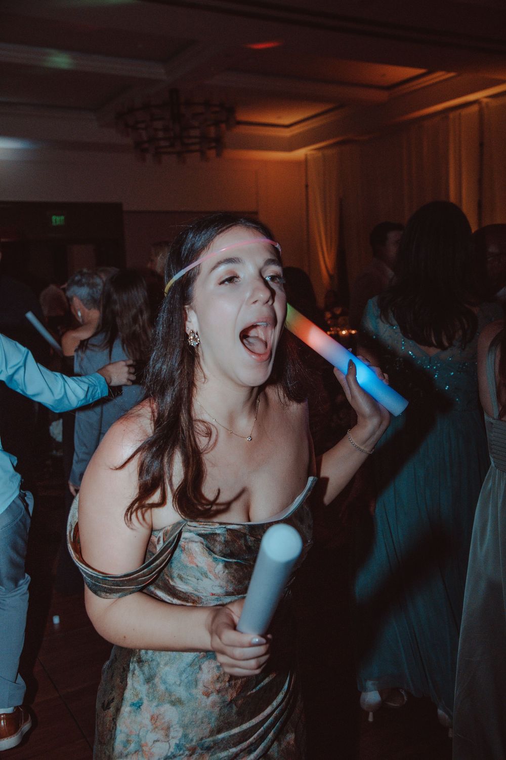 Excited wedding guest dances with glow sticks at a lively wedding reception party on the dance floor.