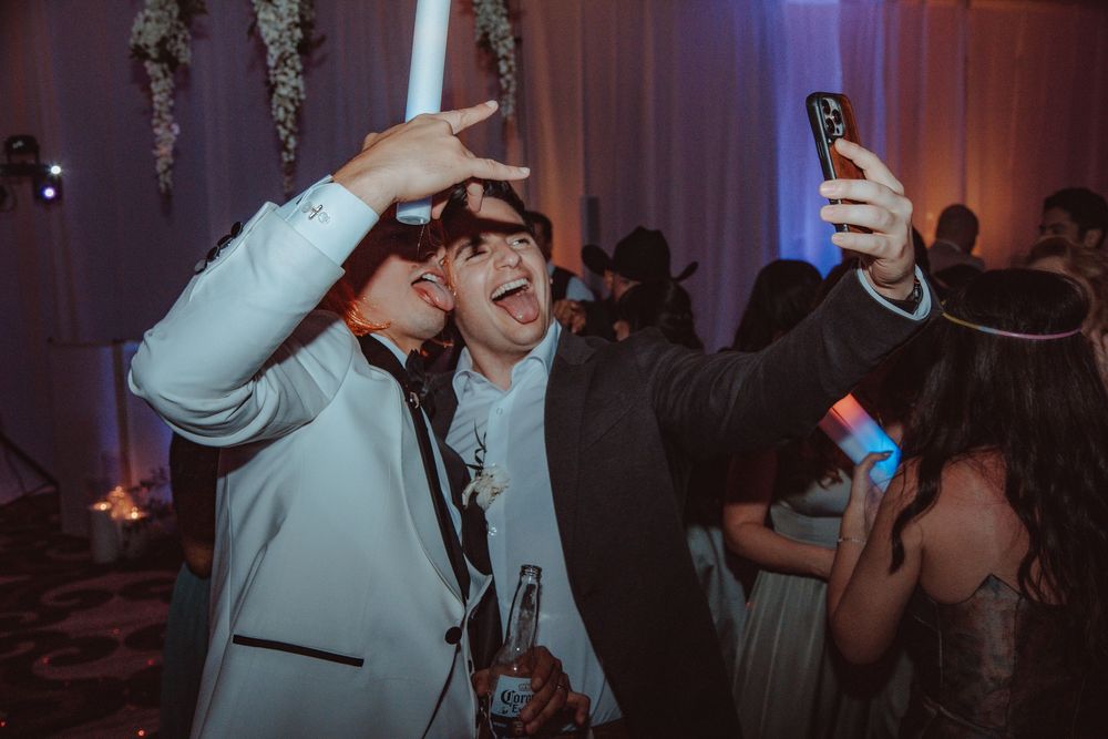 Groom and friend take a selfie together with glow sticks while celebrating at the wedding reception.