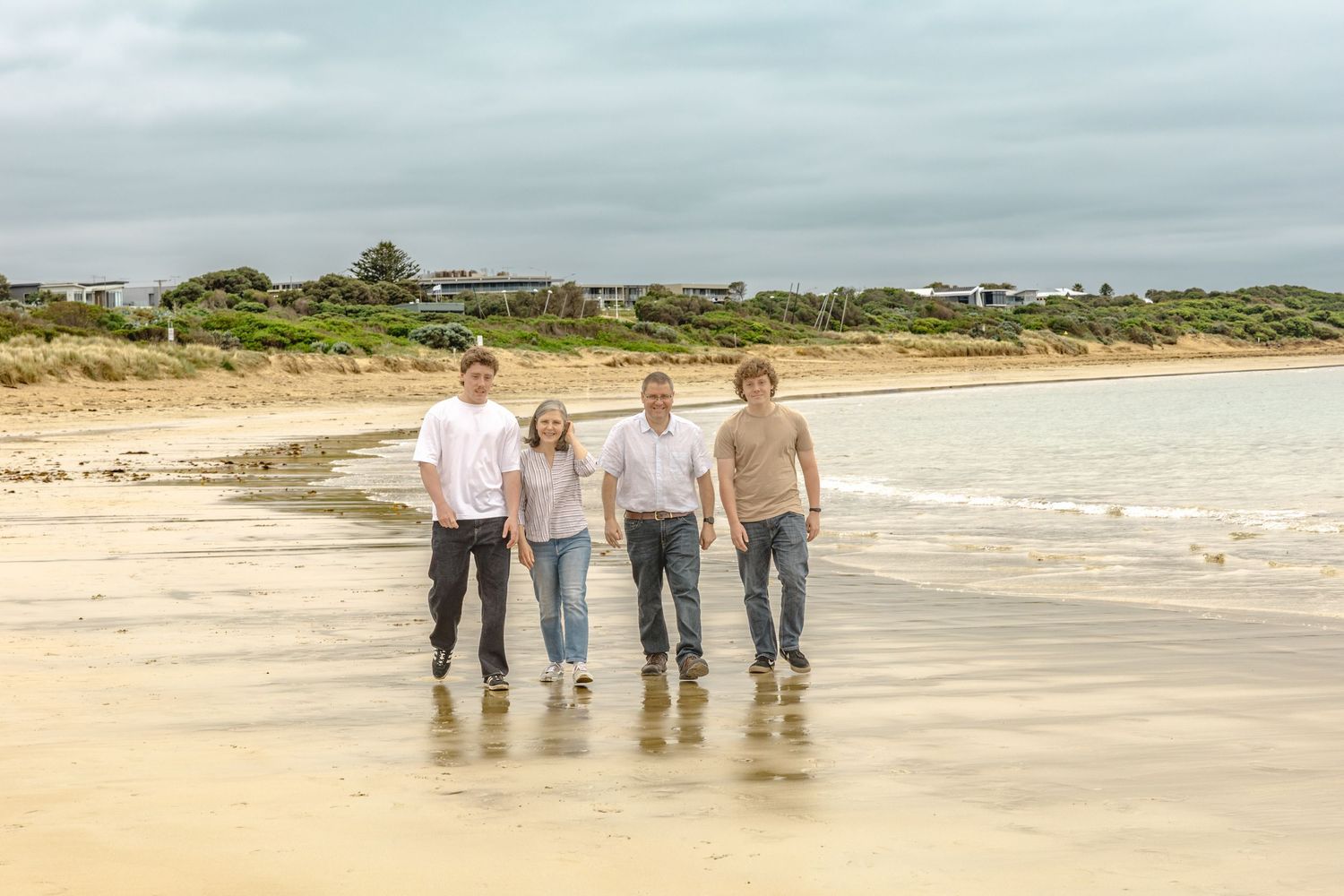 Group walking together along peaceful beach shoreline in coordinated neutral outfits.