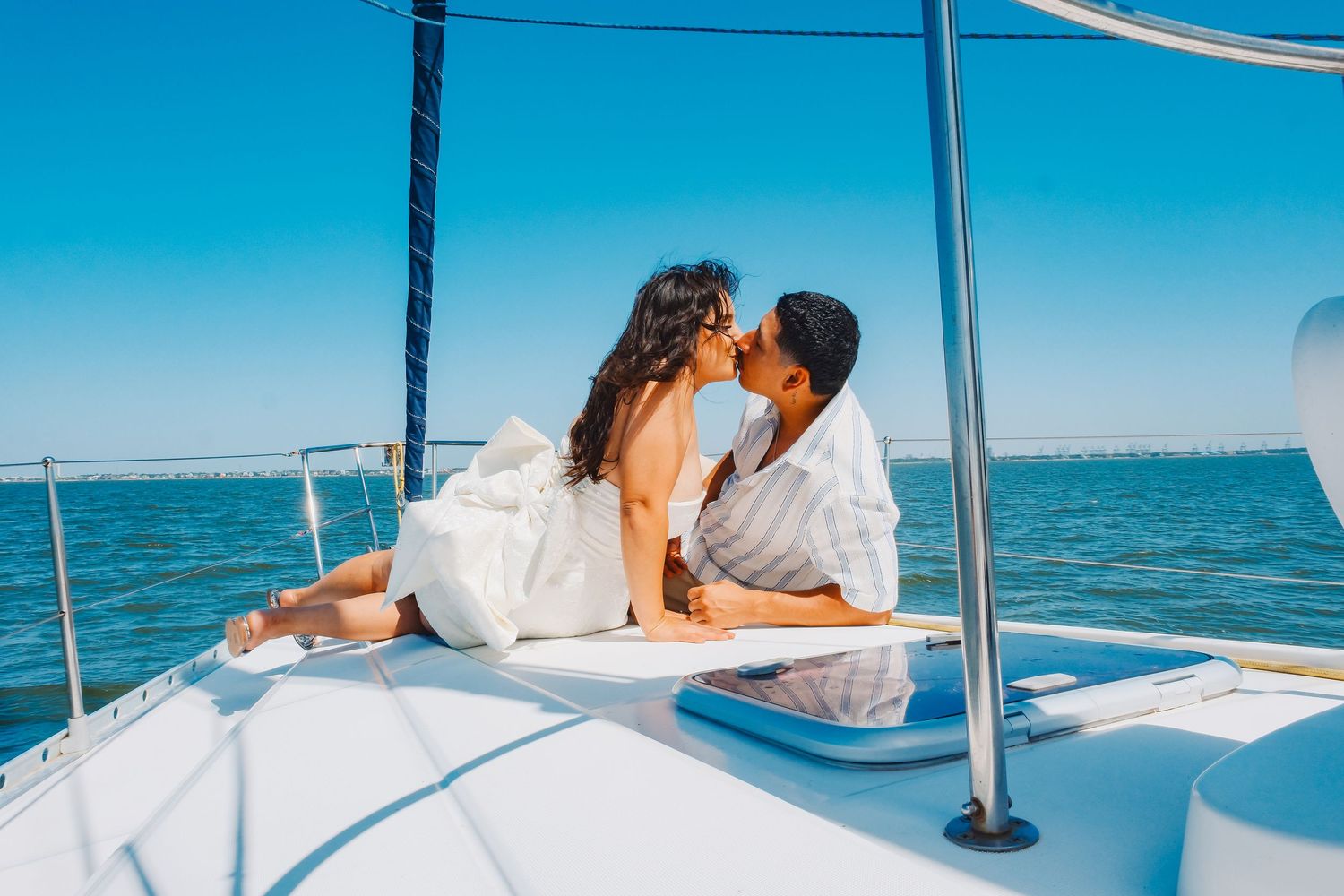Romantic couple sharing a kiss on a luxury sailboat deck on a sunny day with calm blue ocean waters.