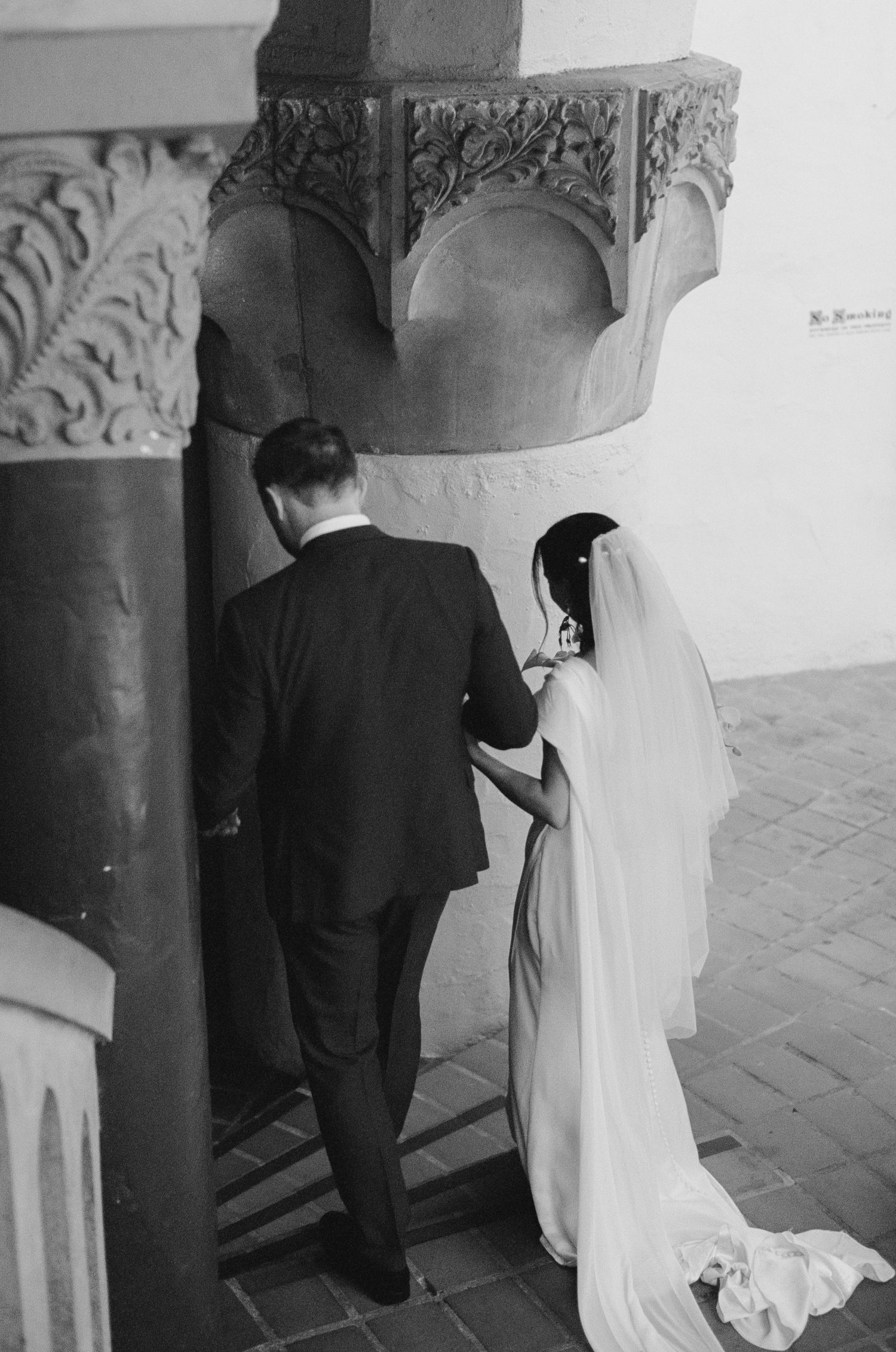 Black and white photo of a bride and groom standing before ornate stone columns at their wedding ceremony.