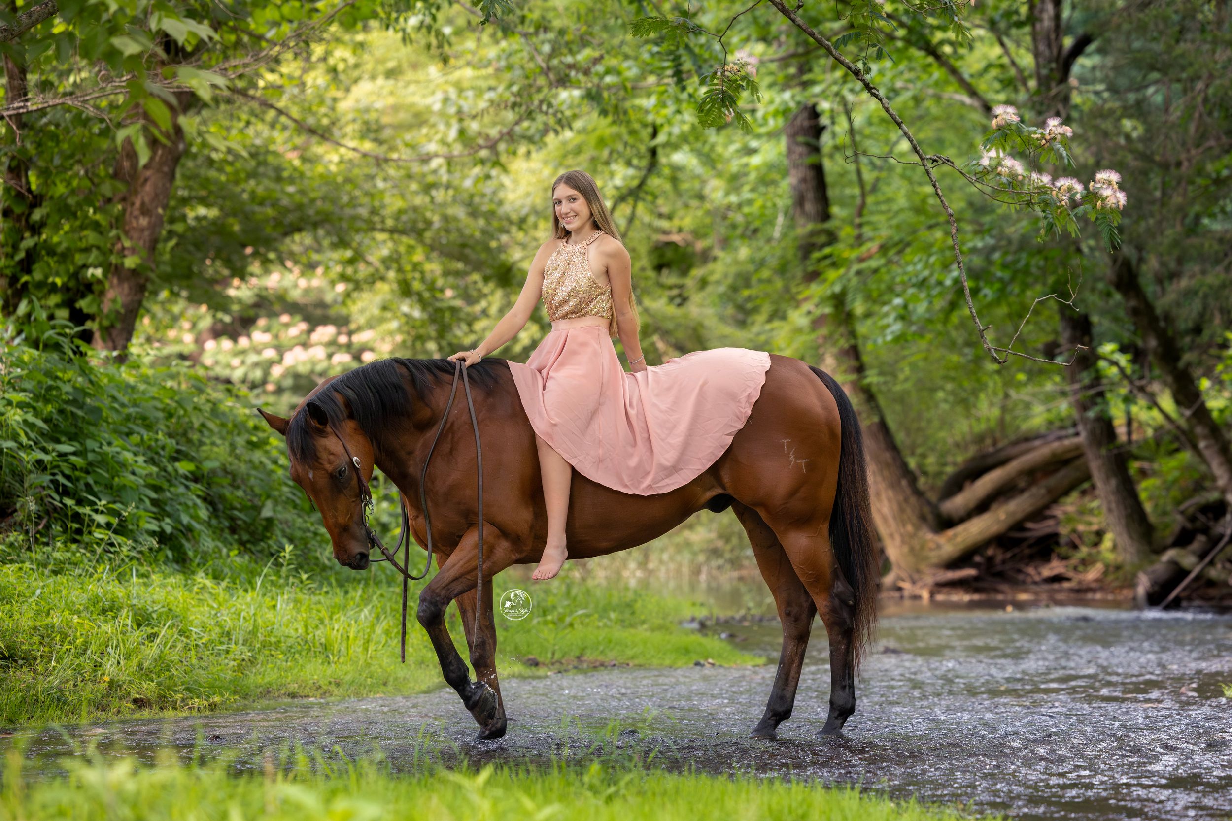 Woman in pink dress riding a brown horse through a lush green forest path.