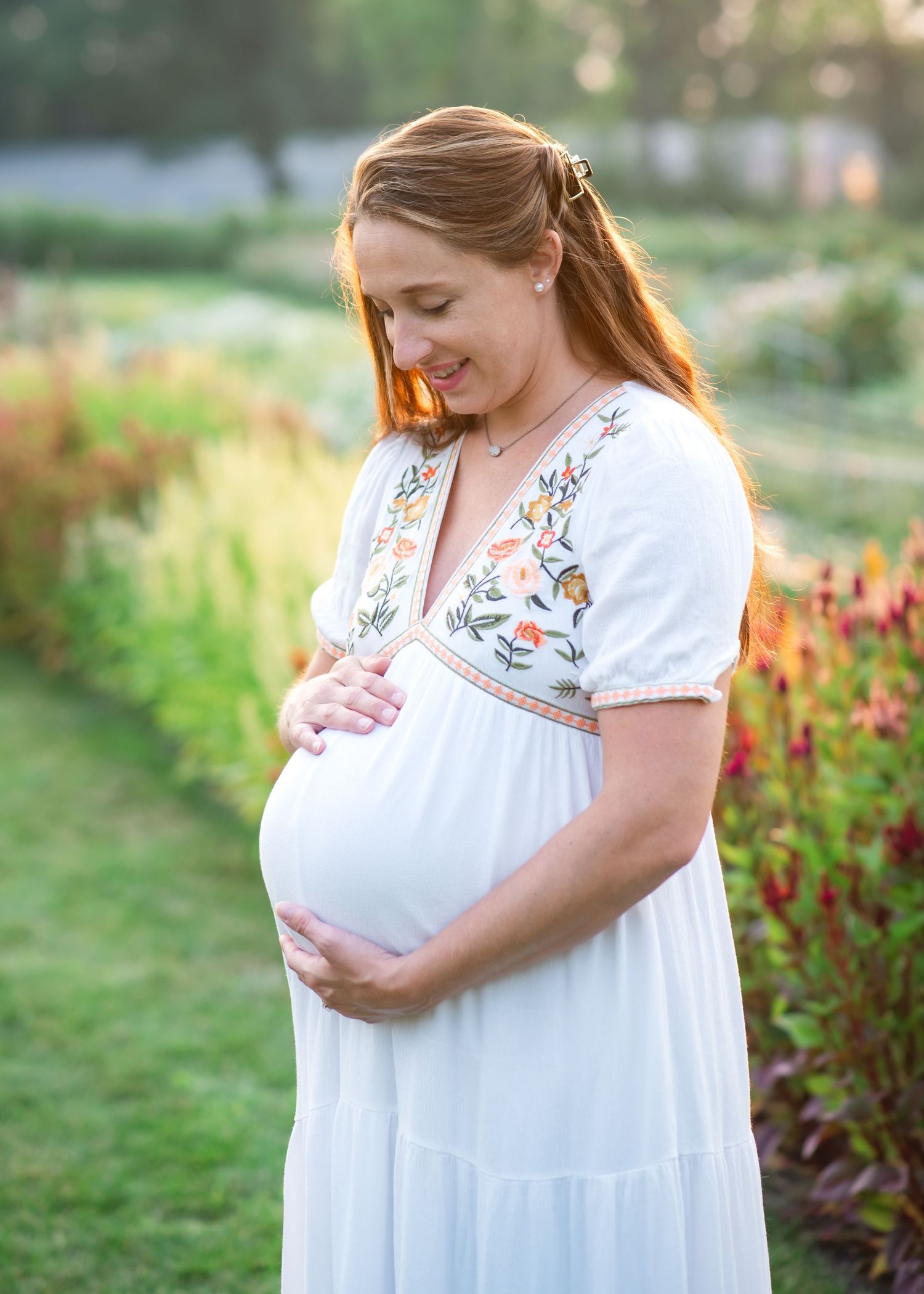 A mother holds her young daughter in a flower field, both smiling and touching foreheads tenderly.
