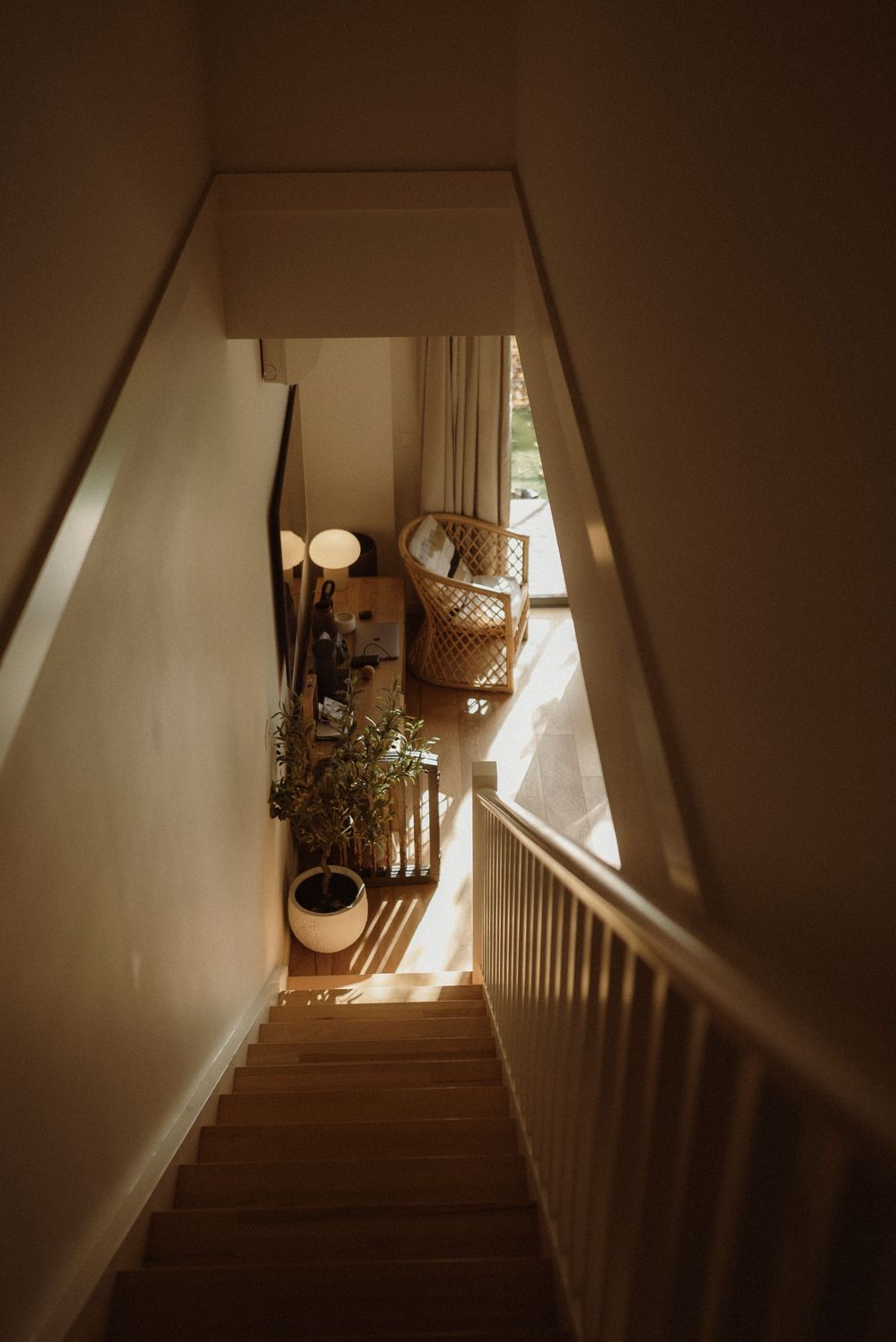 Cozy staircase leading to a sunlit reading nook with a rattan chair, floor lamp, and potted plant in a warm home.