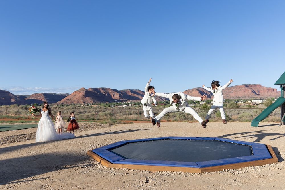 Children in white suits jumping on a trampoline at a wedding with red rock mountains in the background.