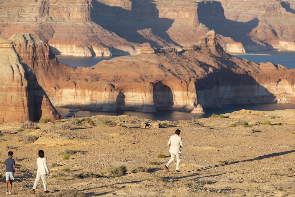 Three people walking near dramatic red rock canyon formations in an arid desert landscape at golden hour.