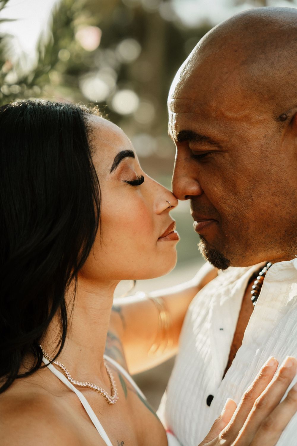 A couple shares a romantic almost-kiss moment outdoors in warm golden light, with the woman wearing a pearl necklace.