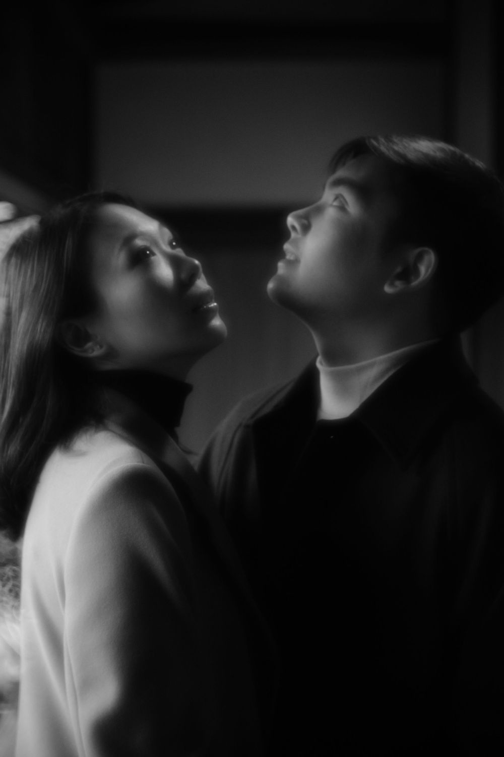 Black and white portrait of a couple gazing upward together in a softly lit intimate moment.