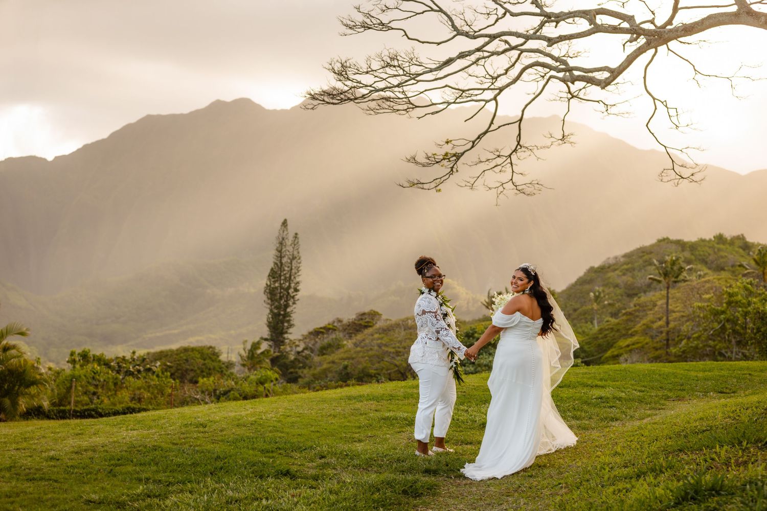 Two brides, one in a lace jacket and whitre slacks.  the other on a off-the-shoulder wedding gown. Hawaii lgbtq wedding photography