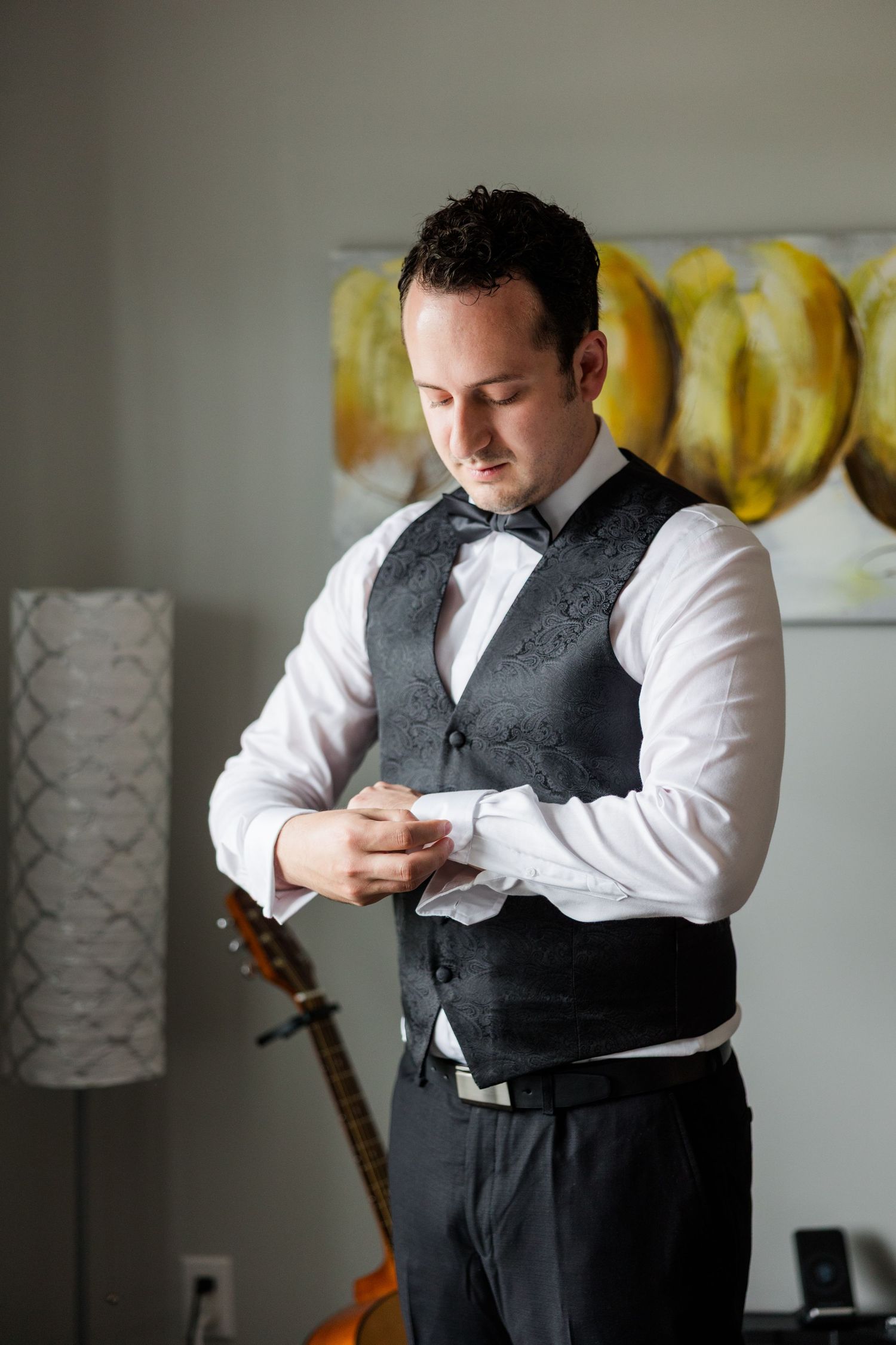 Groom in gray paisley vest and bow tie adjusting cufflinks while getting ready for wedding ceremony.