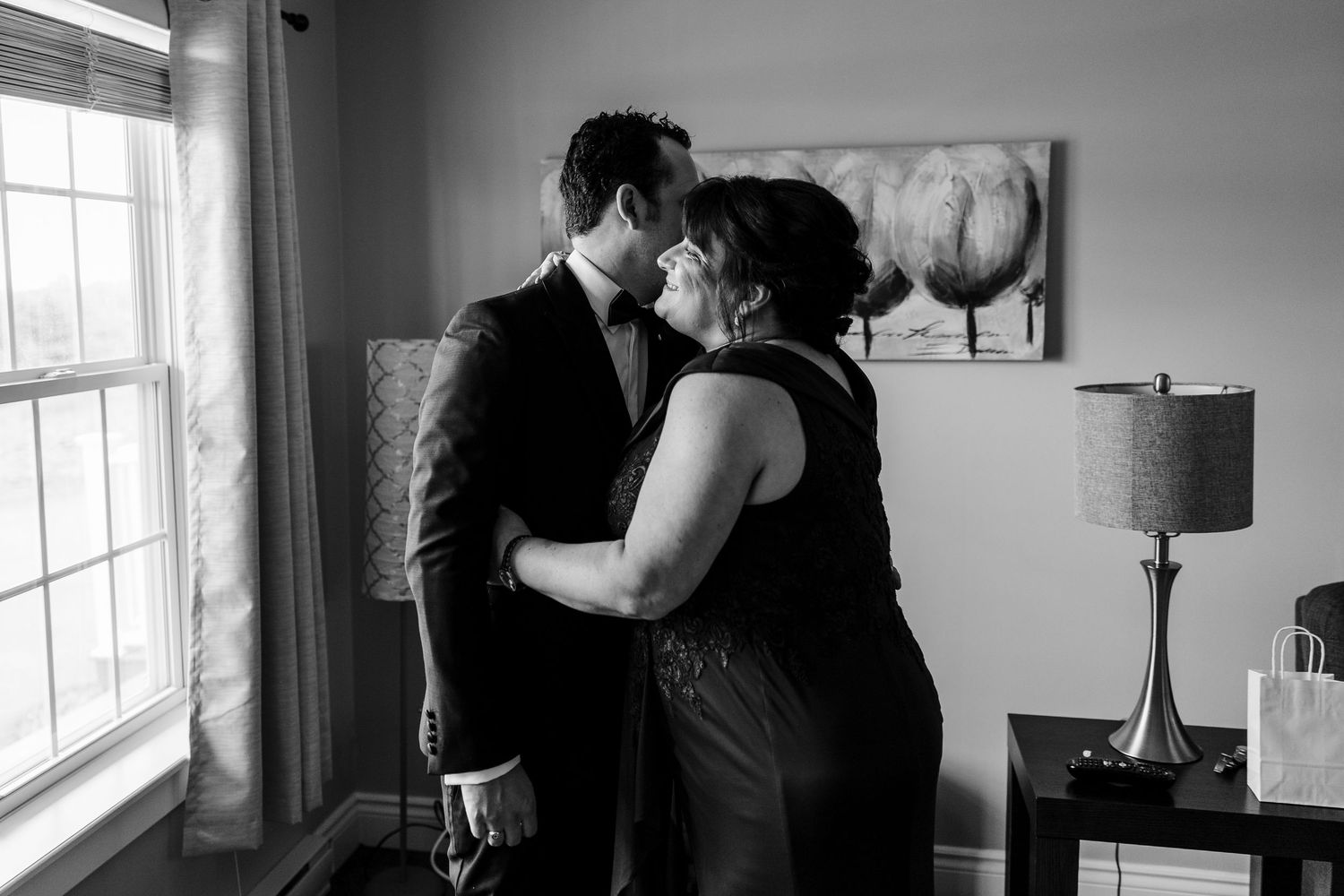 Black and white photo of a groom sharing a tender moment with a woman, likely his mother, before a wedding ceremony.