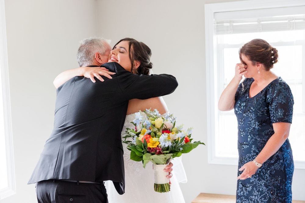Bride hugging her father while emotional mother wipes tears during a touching pre-wedding first look moment.
