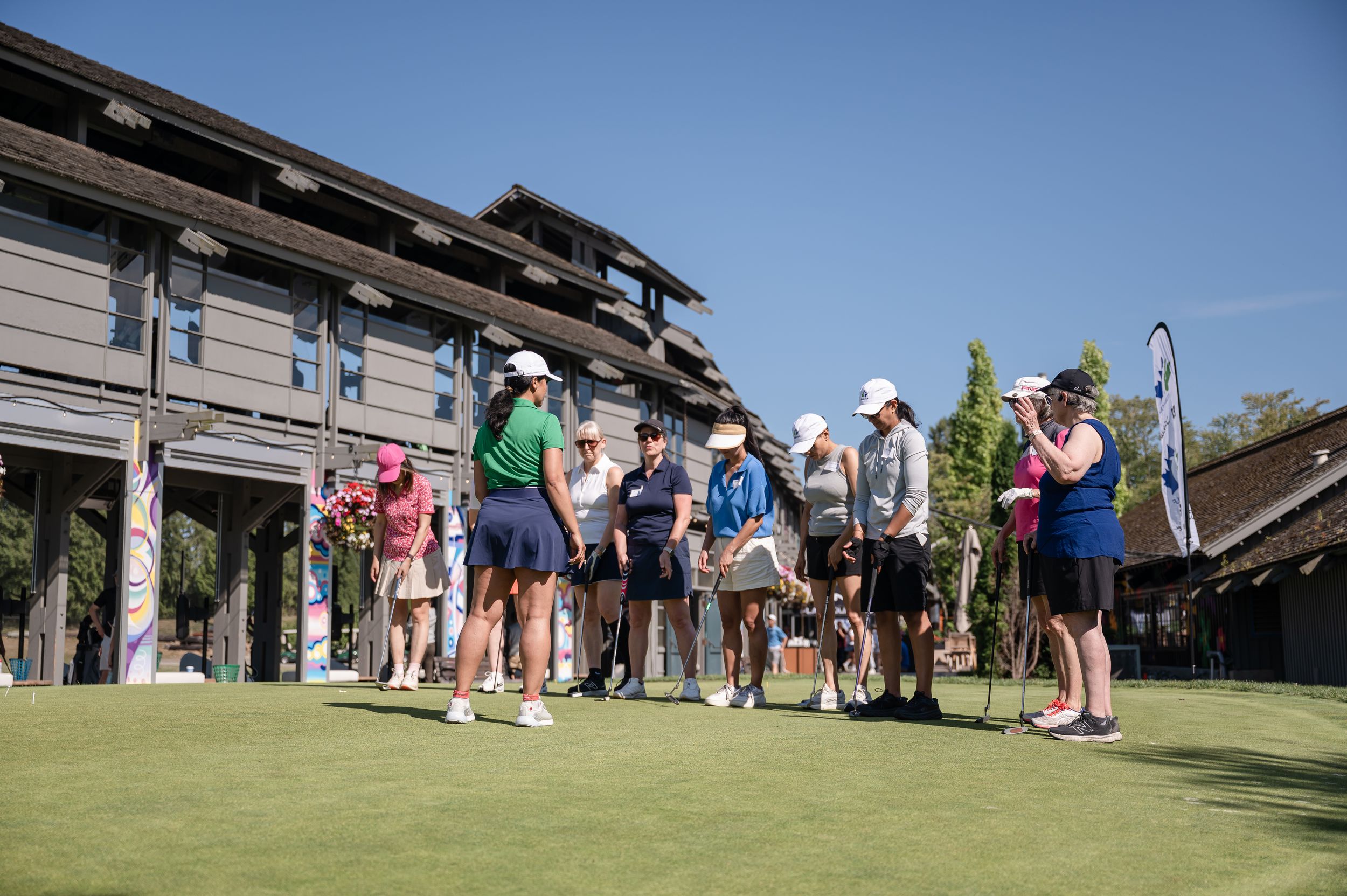 Group of golfers gathered on a sunny golf course near a clubhouse, holding clubs and preparing for a round.