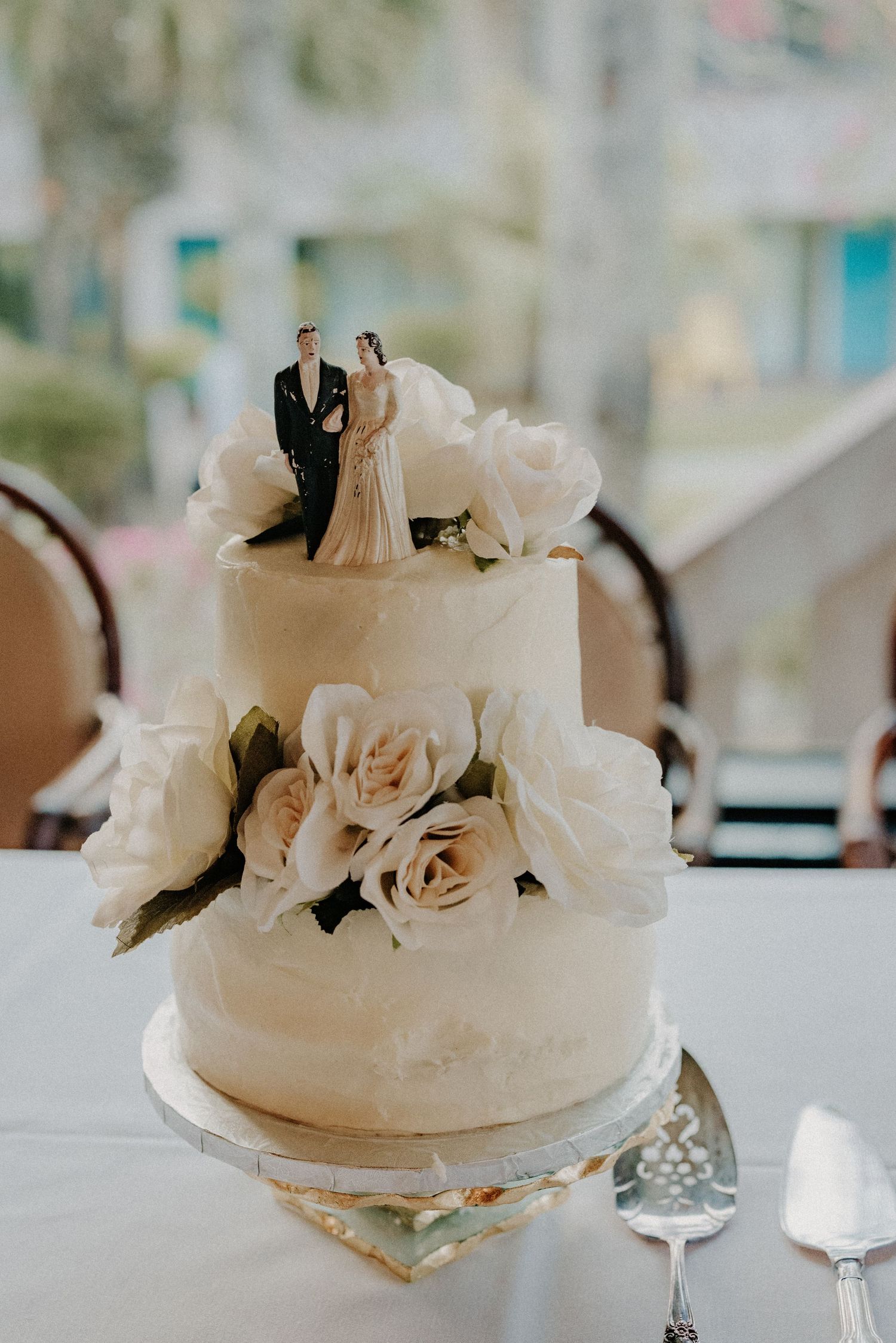 Elegant two-tier white wedding cake with roses and bride and groom cake topper.