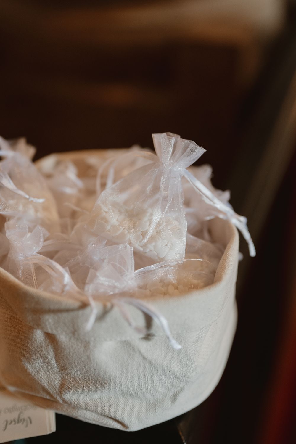 White organza favor bags filled with wedding treats displayed in a linen basket centerpiece.
