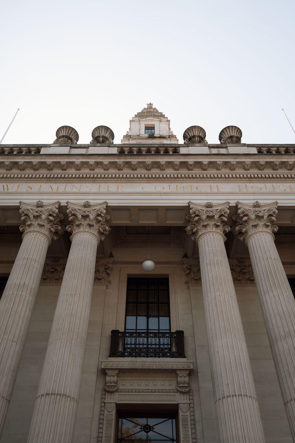 Looking up at Westminster Council House facade with Corinthian columns and ornate roofline details against a pale sky.
