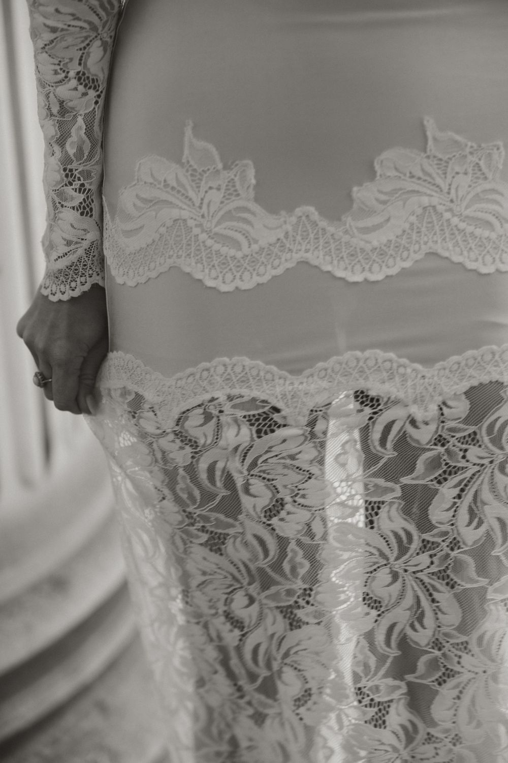 Black and white close-up of intricate lace detailing on a white wedding gown with floral patterns.