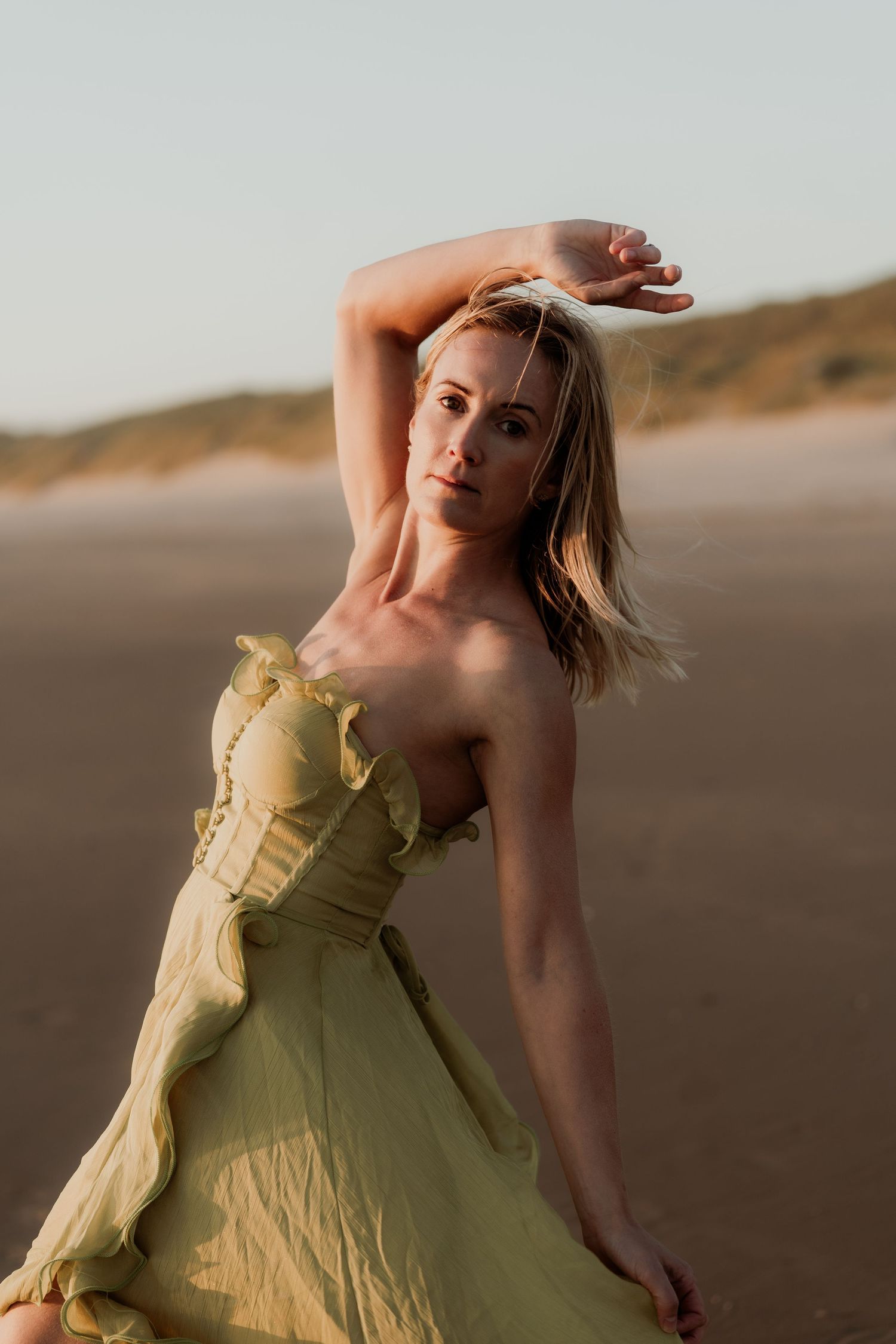 Woman in yellow ruffle dress posing gracefully on a sandy beach at golden hour.