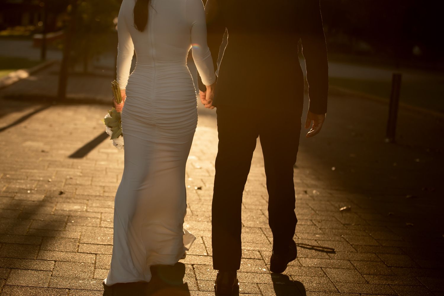 Bride and groom sharing a romantic kiss at golden hour sunset, bride holding white rose bouquet.