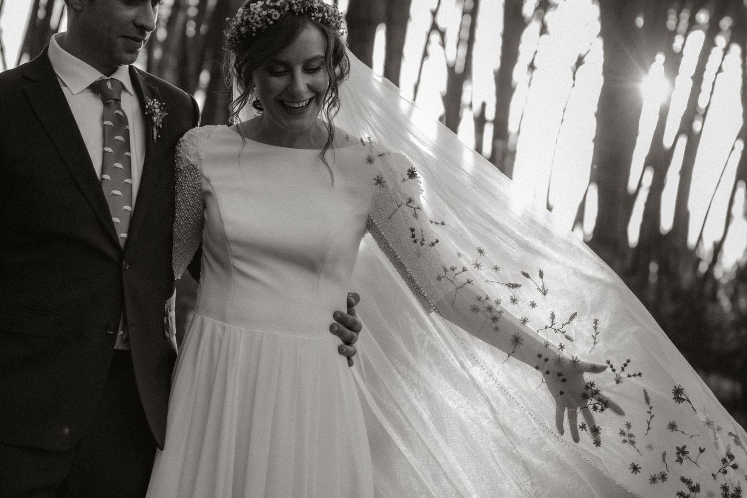 Happy couple laughing outdoors in black and white wedding photo, bride in lace dress holding bouquet.
