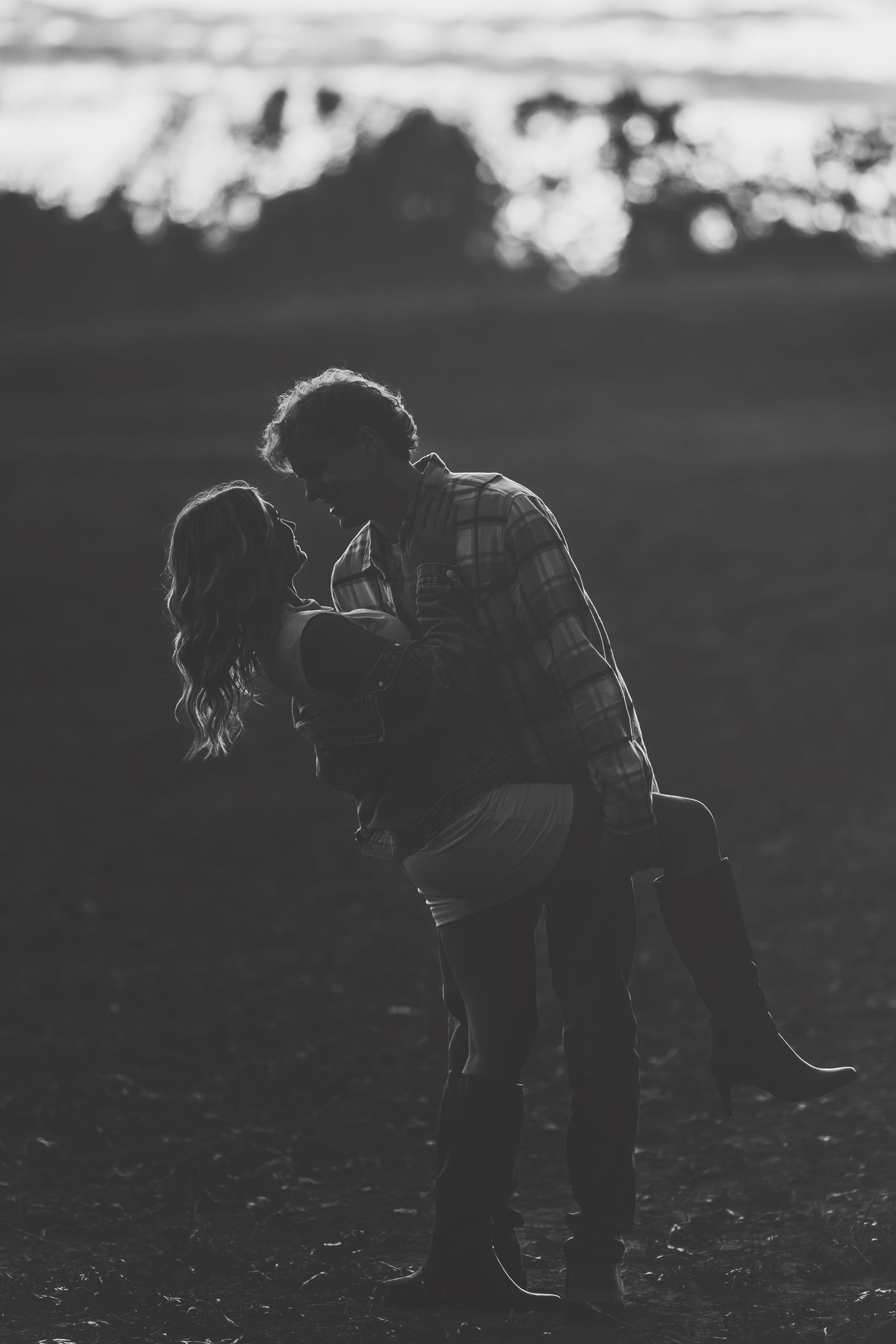 Black and white photo of a couple sharing a romantic dip kiss outdoors at sunset in a field.