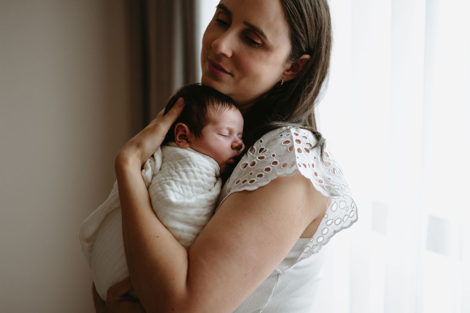 Black and white photo of a mother tenderly holding her swaddled newborn baby close to her face.