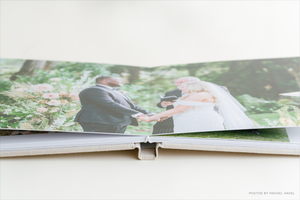 Open wedding photo album displaying a bride and groom ceremony photo in a lush green garden setting.