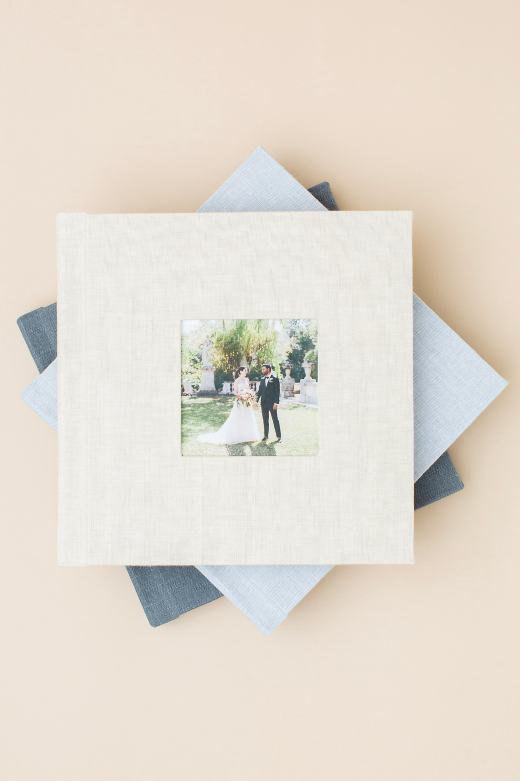 Stack of elegant wedding photo albums with linen covers, featuring a couple portrait on the top cream album.