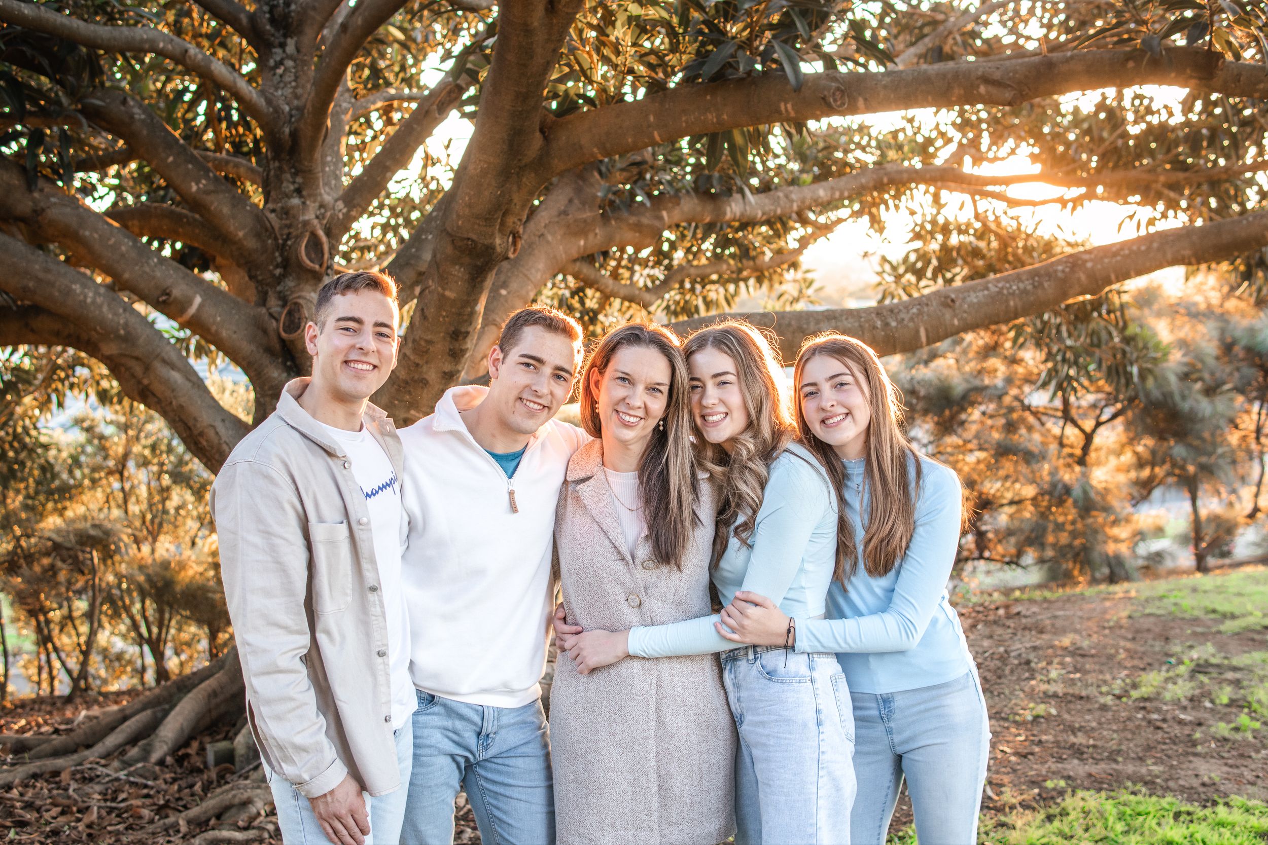 Family of five smiling together under a large tree at golden hour in a park on Beaumont Hills.