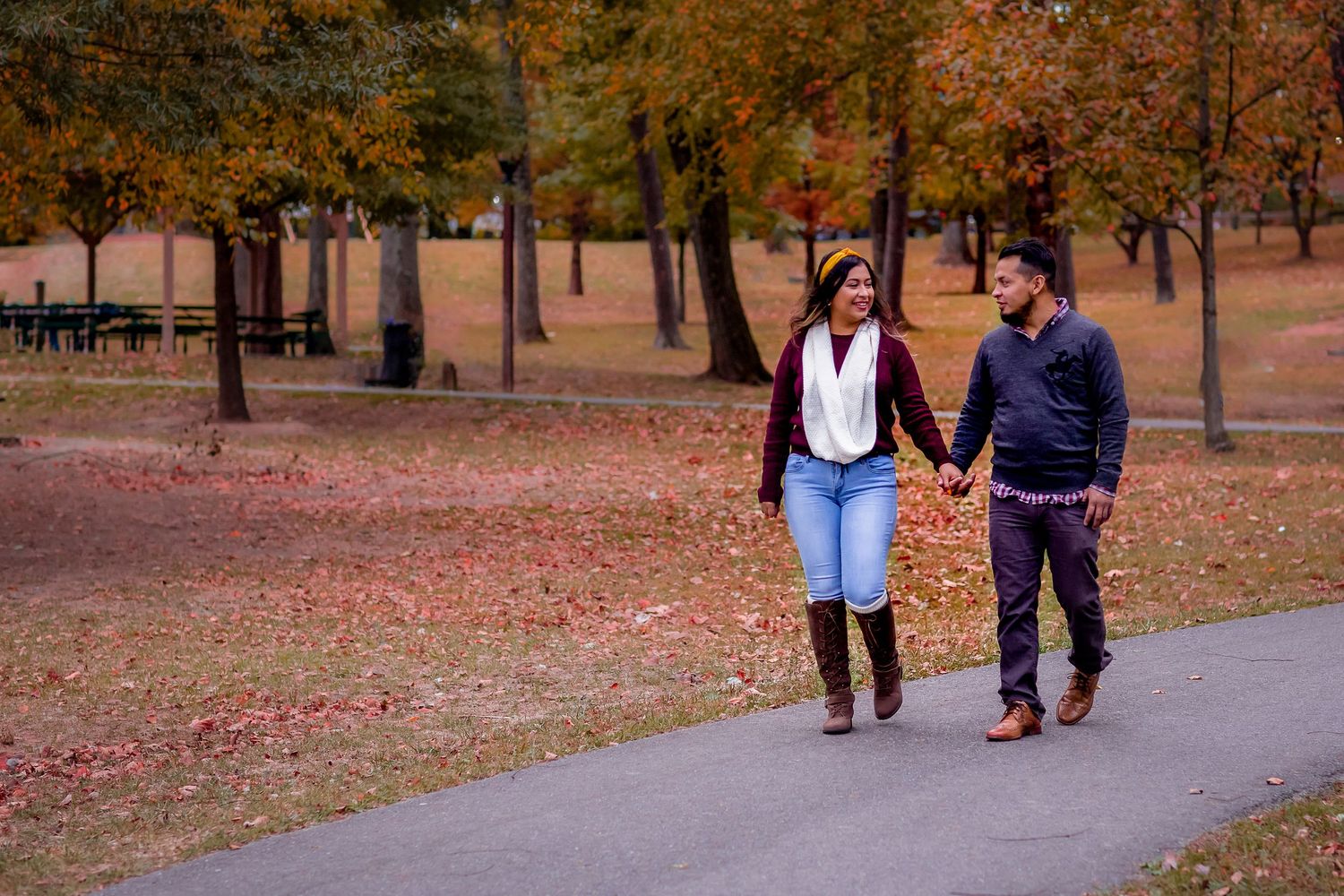 Couple holding hands walking on a path in a park during autumn with colorful fall foliage.