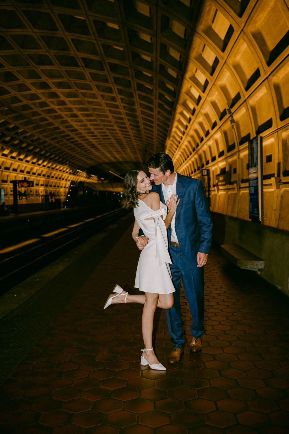 Couple sharing a romantic kiss on a Washington DC Metro subway platform, woman in white dress, man in blue suit.