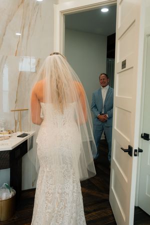 Bride in lace wedding gown and veil shares an emotional first look moment with a man in a light blue suit.