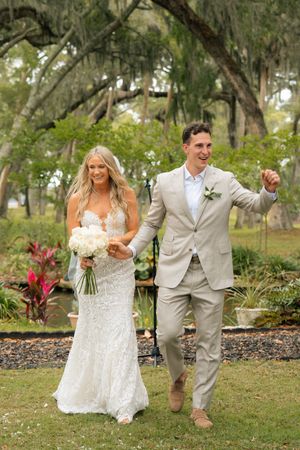 Joyful bride and groom walking together outdoors after wedding ceremony, surrounded by lush greenery and Spanish moss trees.
