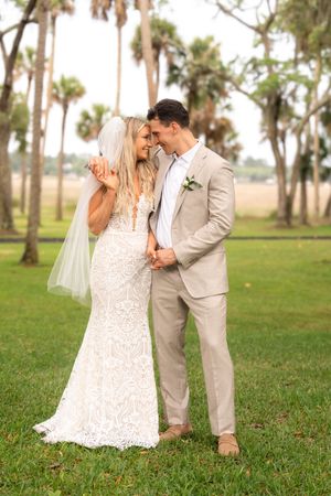 Happy bride and groom embracing outdoors on green grass with palm trees at wedding.