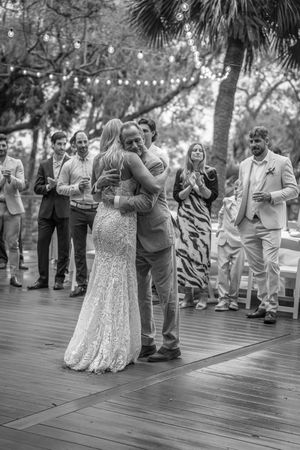 Black and white photo of a bride and groom sharing their first dance at an outdoor wedding reception with guests watching.