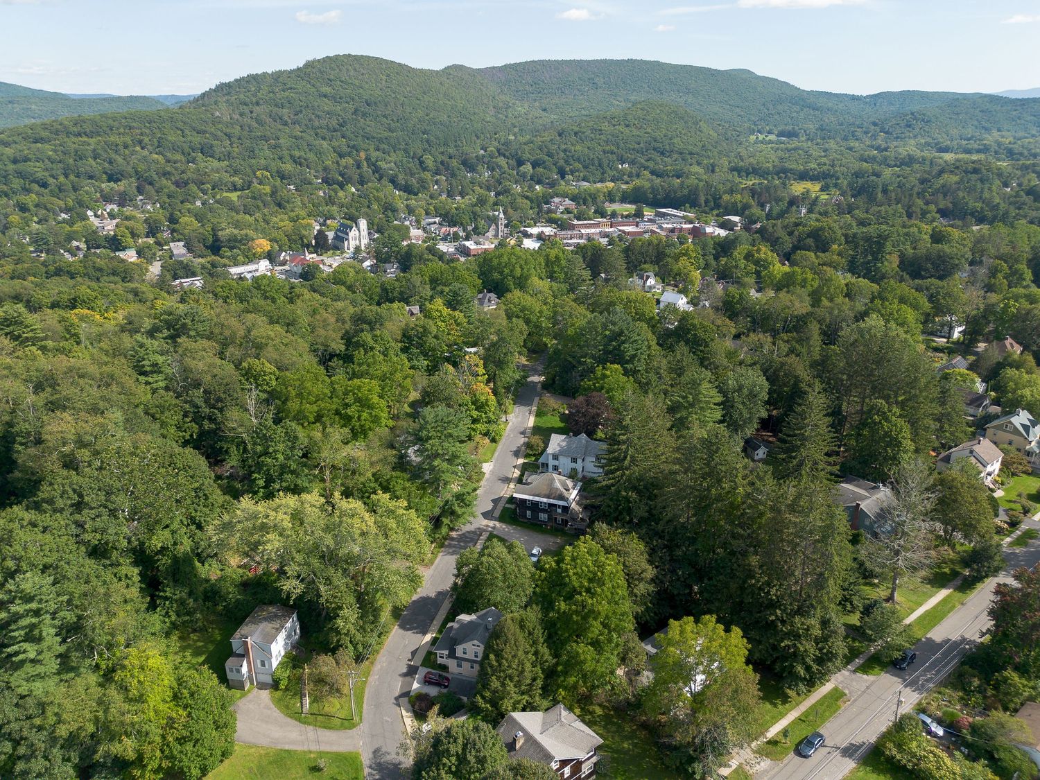 Aerial view of a New England town nestled among green hills and tree-lined streets.