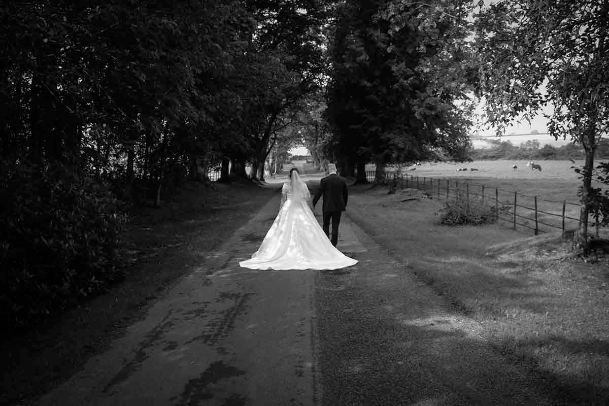 Black and white photo of the bride and groom walking down the tree-lined driveway at Blaithwaite House wedding venue near Wigton