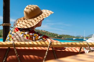 Person in straw hat and floral shirt enjoying a tropical ocean view from a wooden sailboat deck.