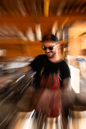 Man in black t-shirt and sunglasses smiling, captured with dramatic zoom blur effect in warm-toned setting.