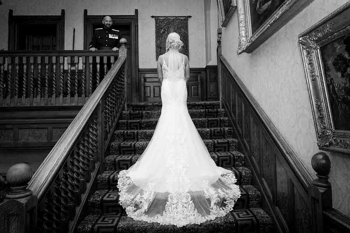 Bride in elegant lace mermaid wedding gown stands on grand staircase at Armathwaite Hall near Keswick