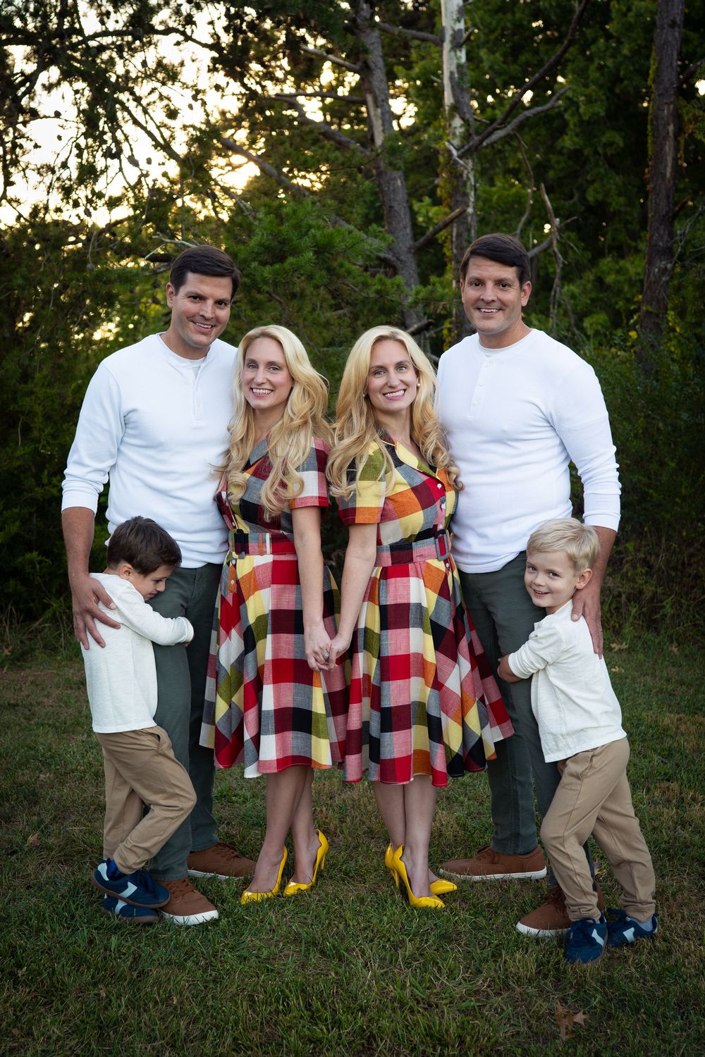 Two identical twin couples with matching outfits pose with their young children outdoors.