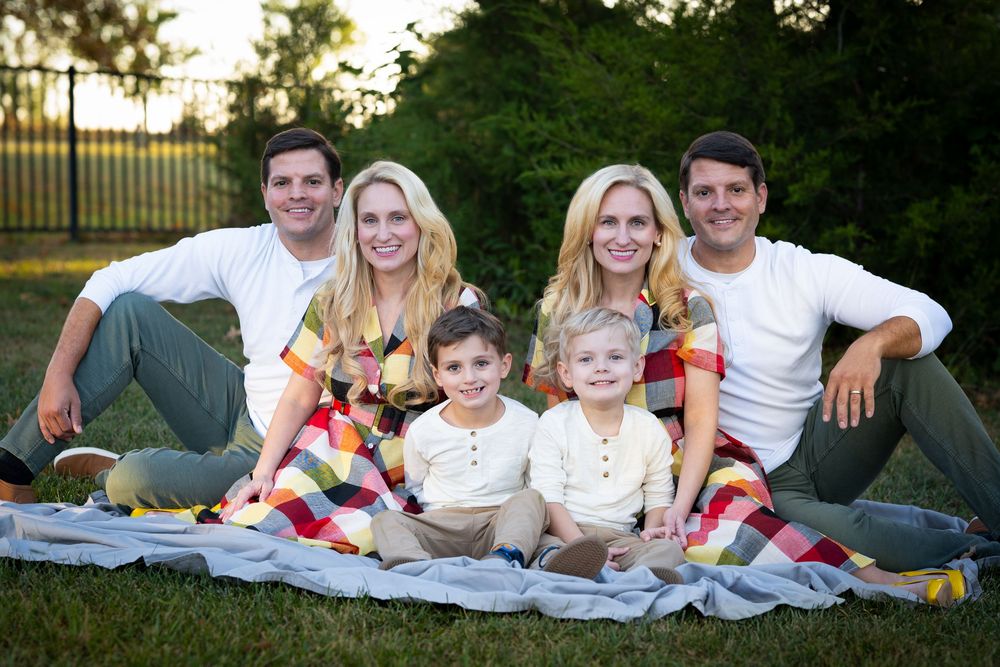 Two couples with two young children sitting on a blanket outdoors for a family portrait session.