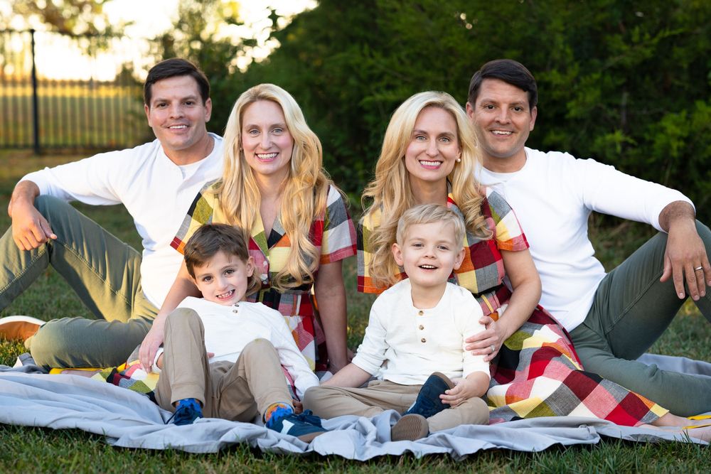 Two families with young children smiling together on a blanket during an outdoor photo session.