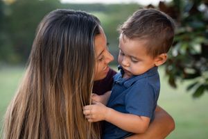 Loving mother holding young toddler son close outdoors in green park setting.