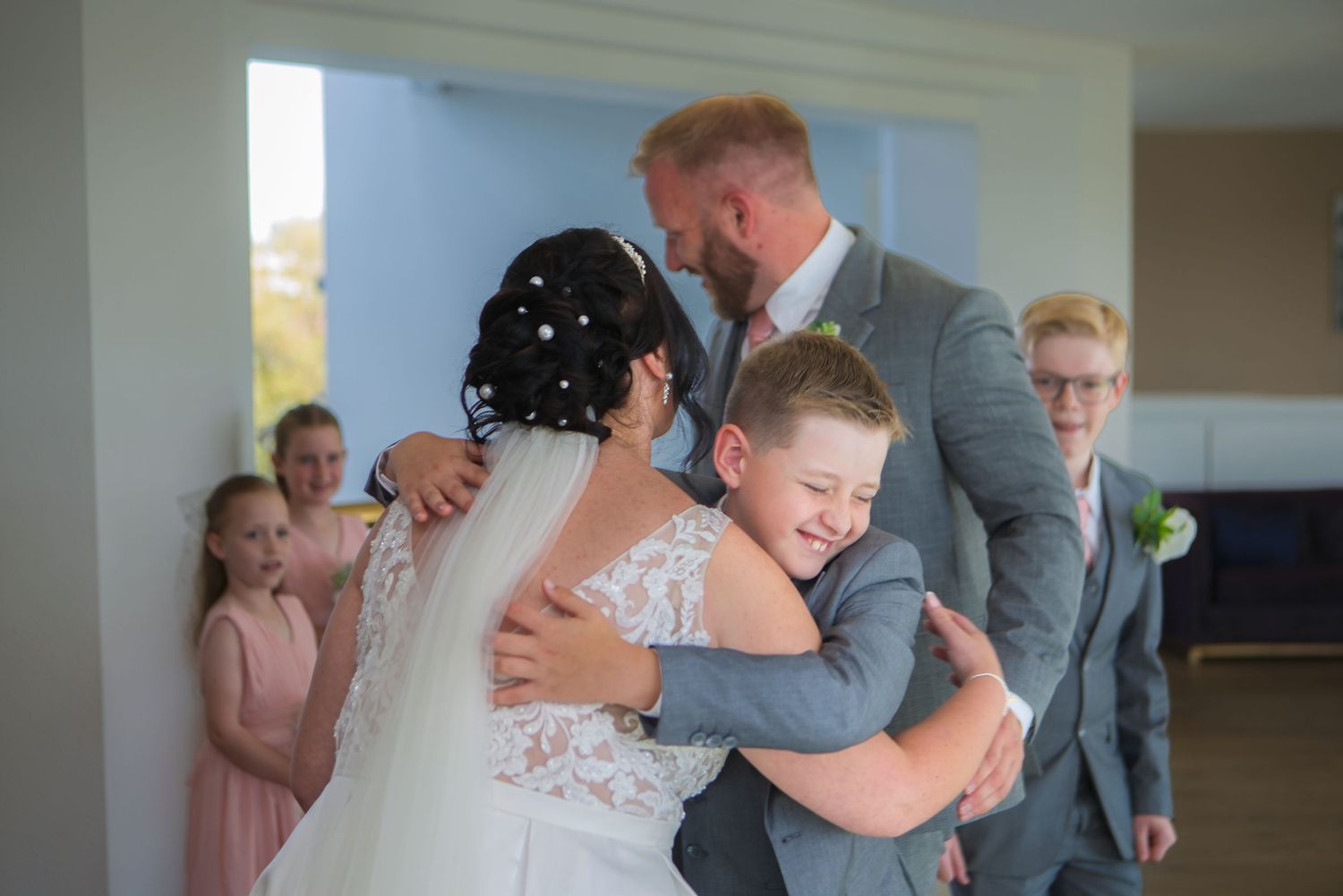 A joyful wedding scene with a bride and groom embracing children in formal attire, capturing a heartfelt family moment.