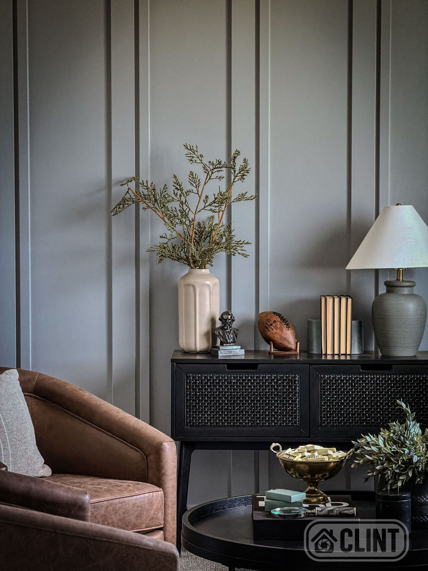 Sophisticated gray paneled accent wall with black console table, lamp, and brown leather armchair decor.