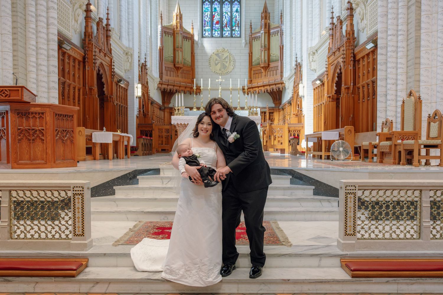Bride and groom posing happily at the altar of an elegant cathedral with ornate wooden details.